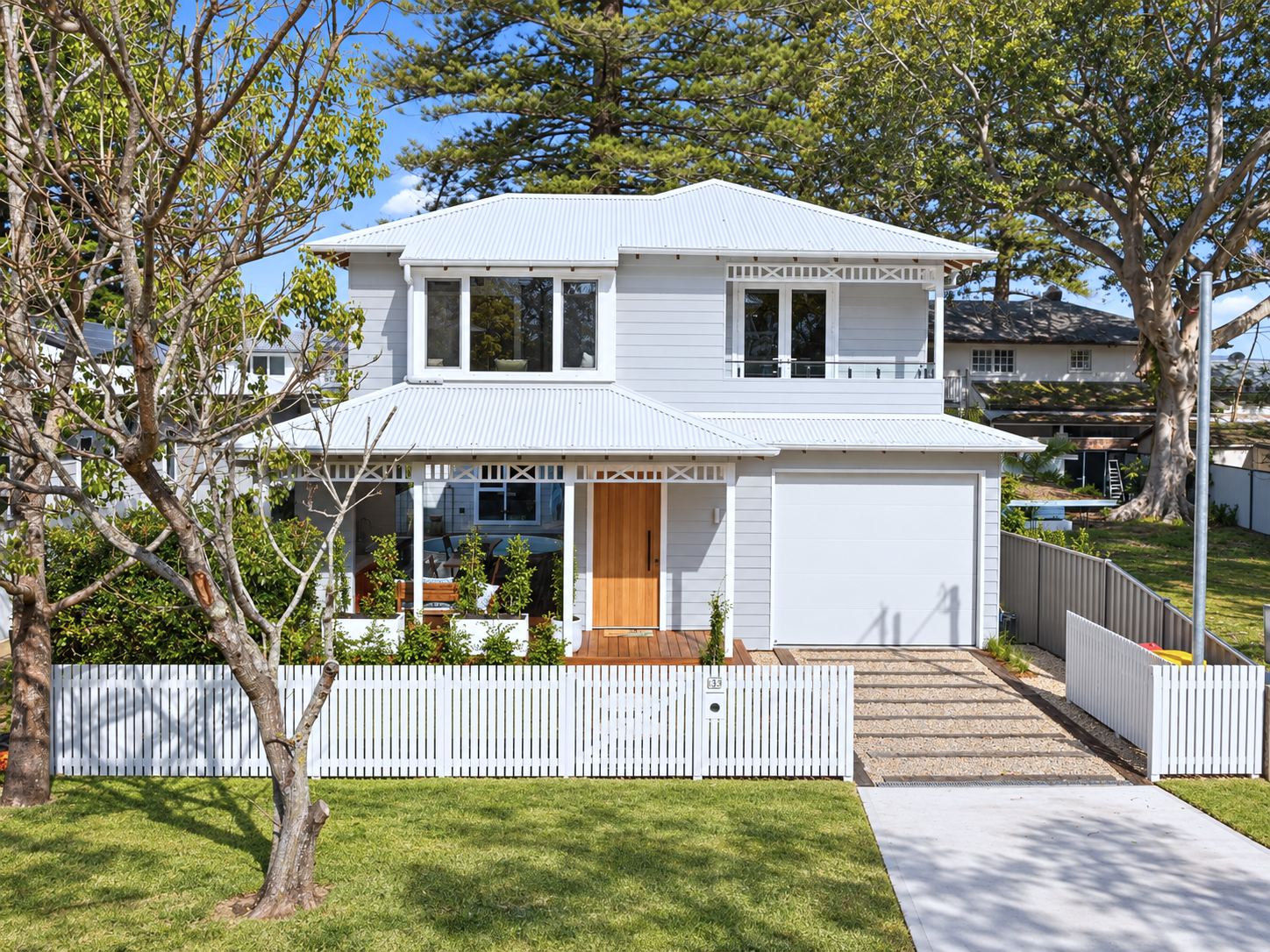 The white weatherboard two-storey facade behind a picket fence, framed by Norfolk pines